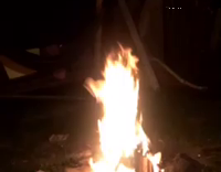 two guys jump over bonfire