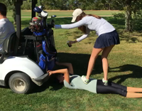 girl holding on to golf cart while friend spills beer on her